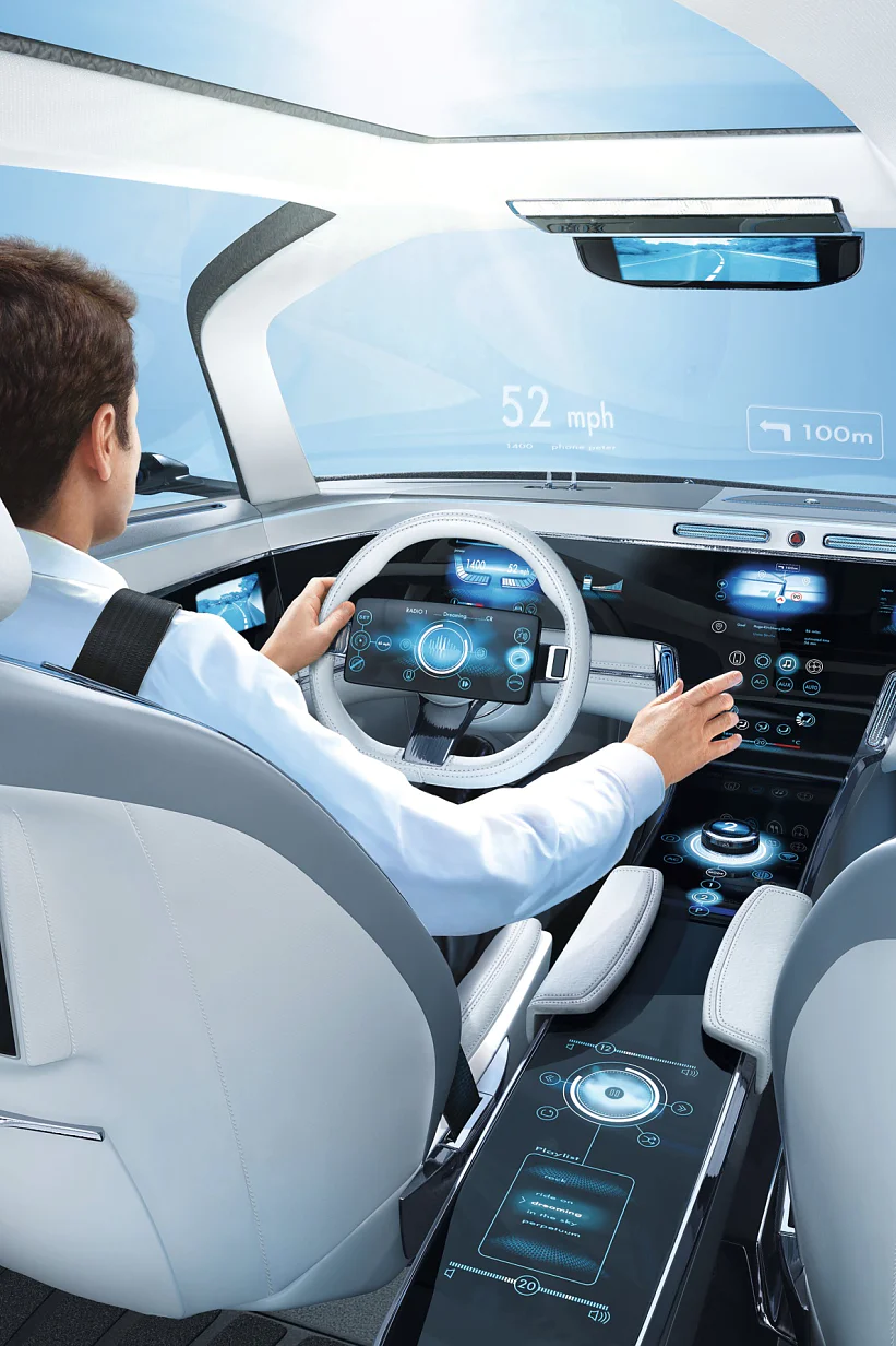 A person is seated in a futuristic car interior featuring advanced digital displays on the dashboard, steering wheel, and seatback. The car shows a speed of 52 mph and distance of 100m on the windshield display. The interior is sleek and modern, with tesa tape seamlessly integrating various components for a streamlined appearance. (This text has been generated by AI)