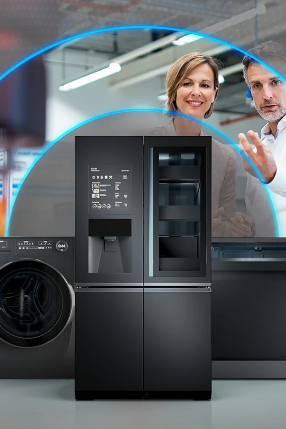 Two people gesturing towards sleek black kitchen appliances, such as a washing machine, refrigerator, and dishwasher. The image showcases a modern setting with blue light arcs surrounding the appliances. (This text has been generated by AI)