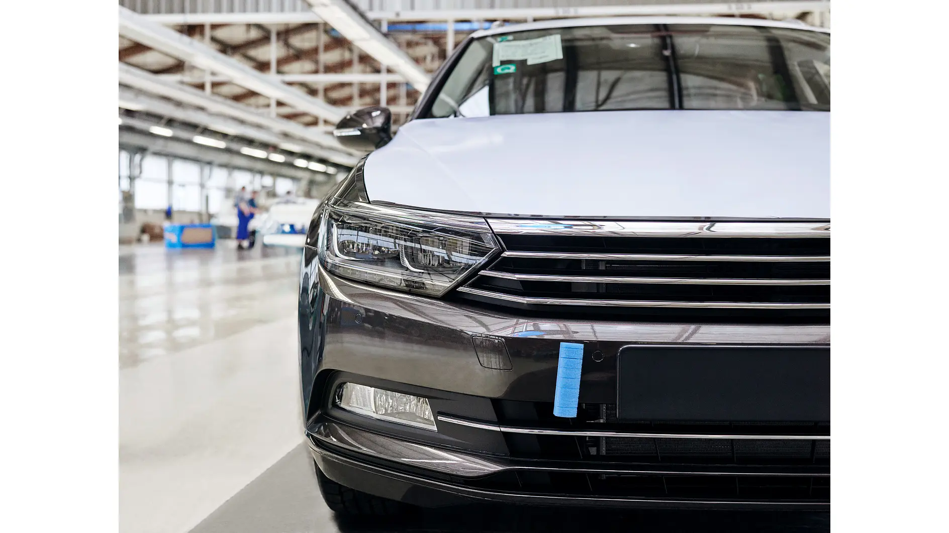 front view of a black and white car inside a spacious industrial facility with workers in the background tesa (This text has been generated by AI)